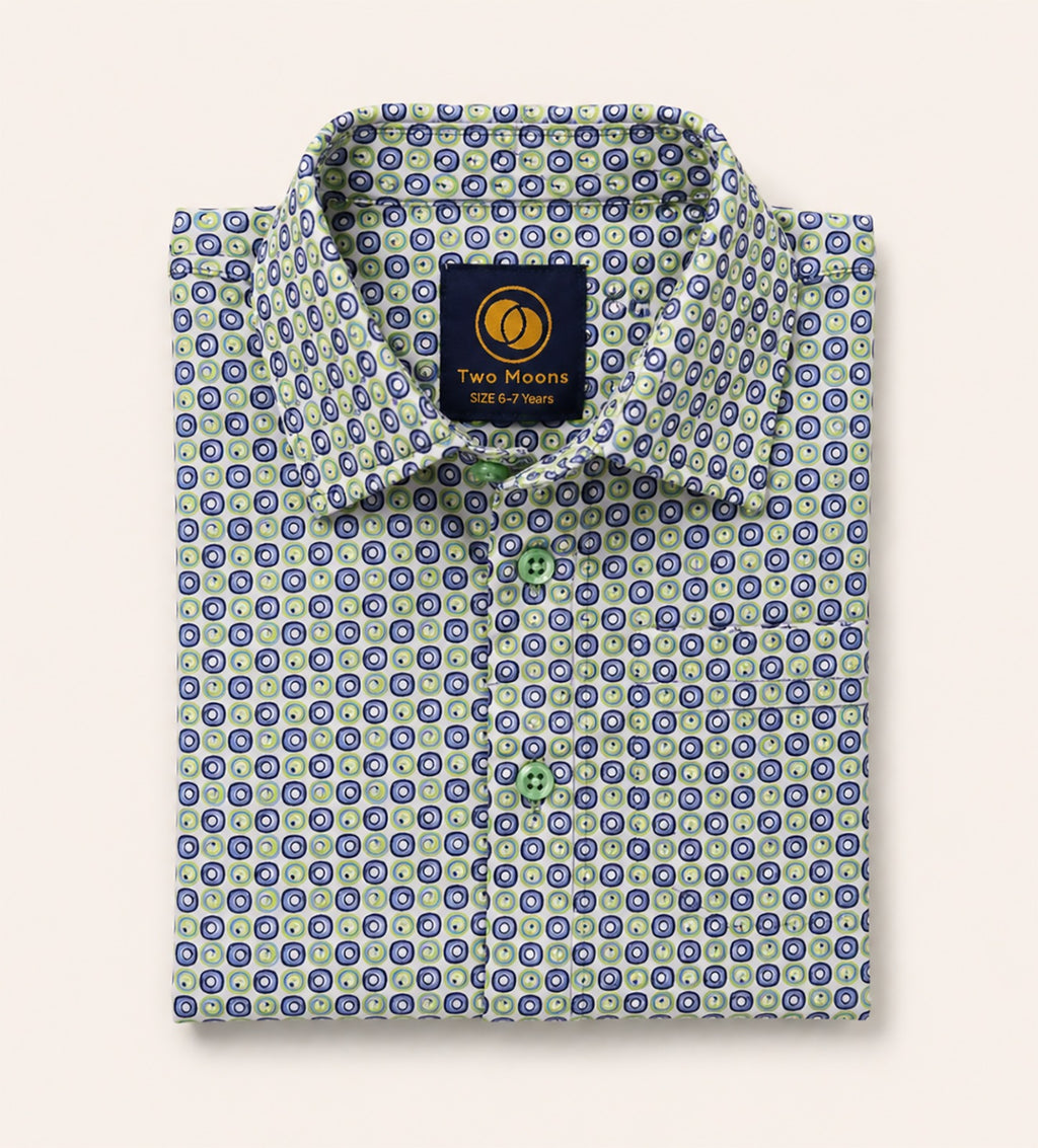 Neatly folded kids button-down shirt highlighting the intricate green and navy circular geometric pattern and matching light green buttons.