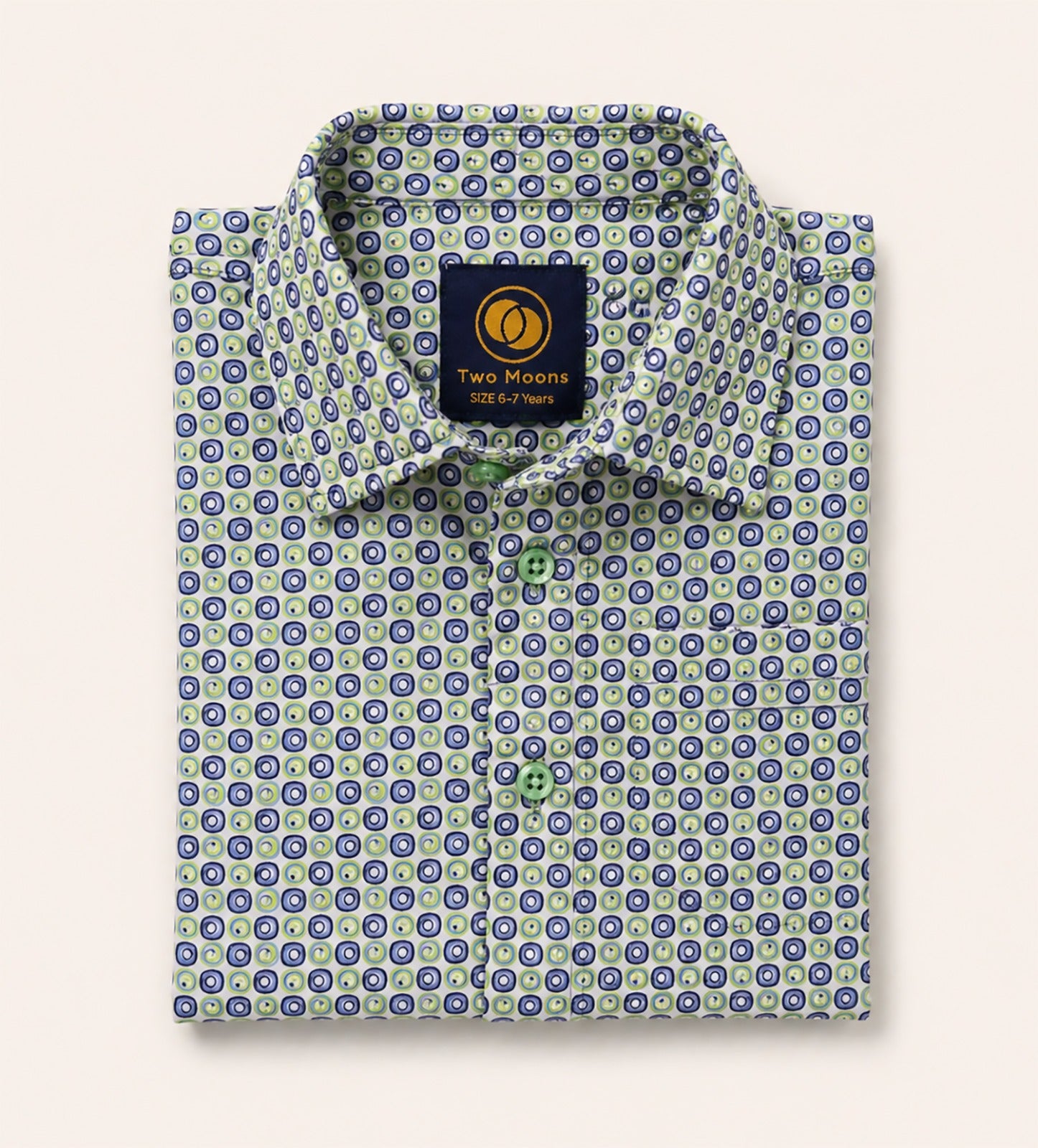 Neatly folded kids button-down shirt highlighting the intricate green and navy circular geometric pattern and matching light green buttons.