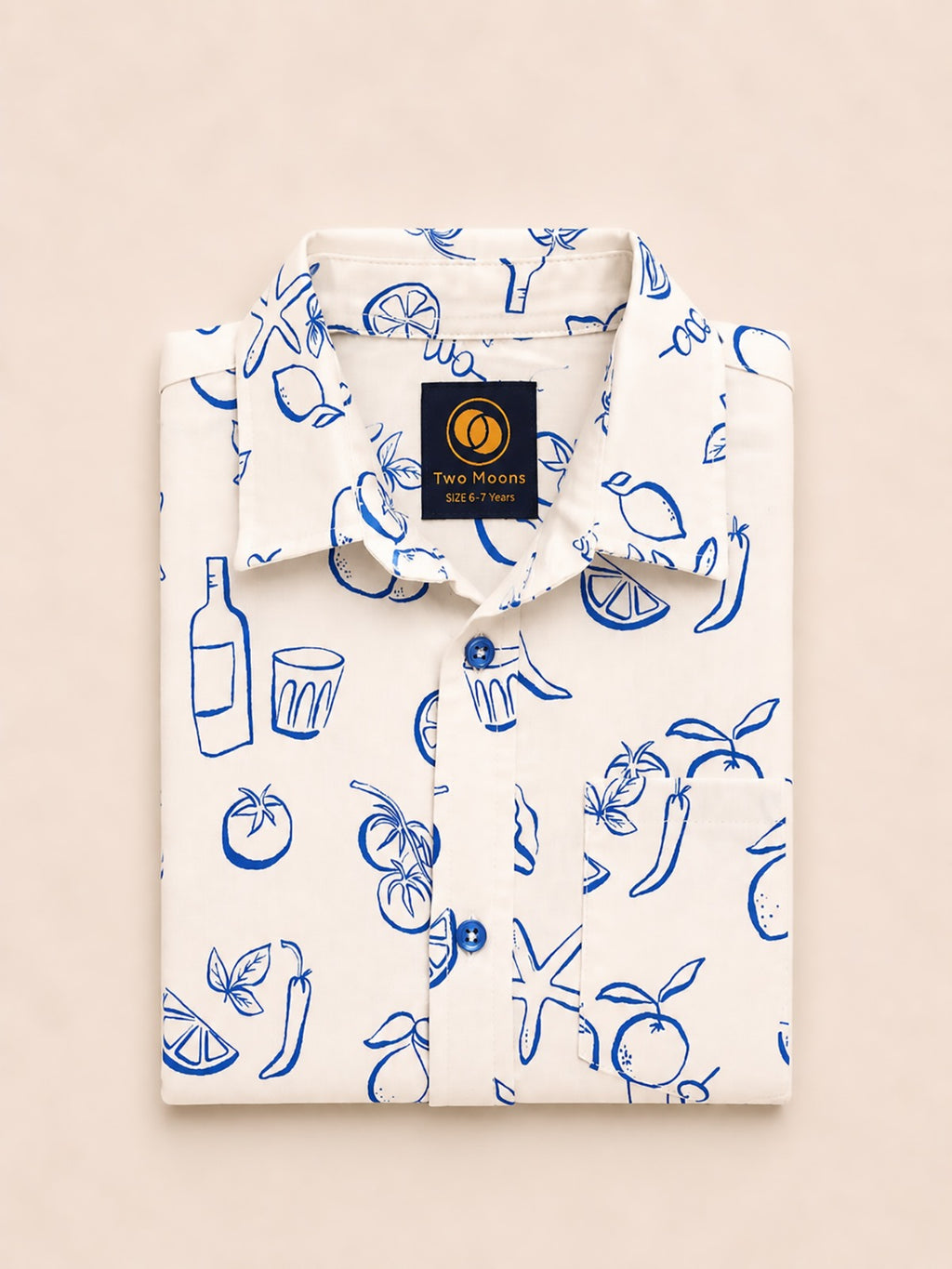 Neatly folded white kids button-down shirt highlighting the blue line-art lemon, tomato, and starfish print alongside bright blue buttons.