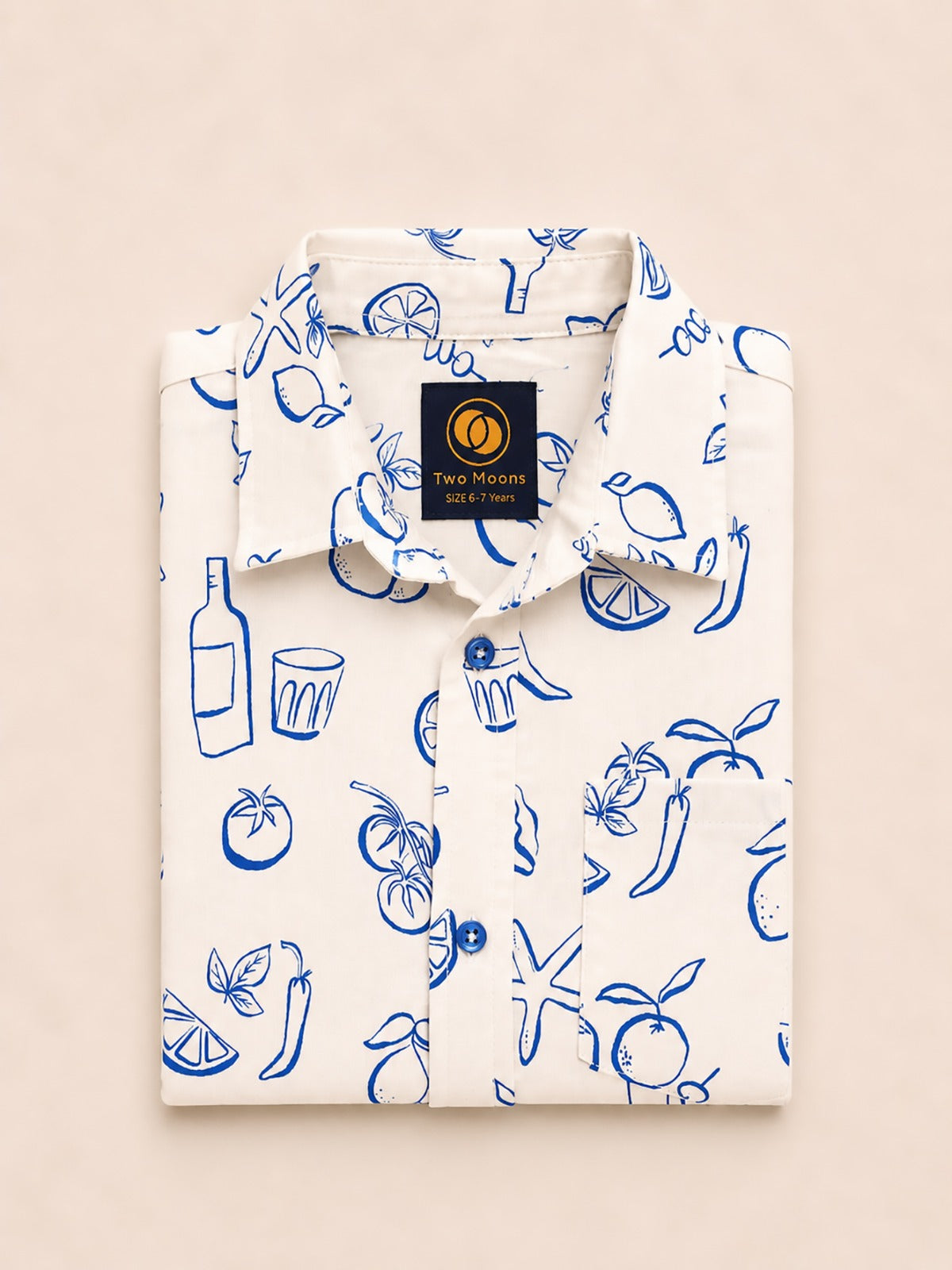 Neatly folded white kids button-down shirt highlighting the blue line-art lemon, tomato, and starfish print alongside bright blue buttons.