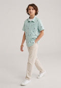 A kid wearing a light mint green kids short-sleeve button-down shirt showing the subtle, repeating small bird print.
