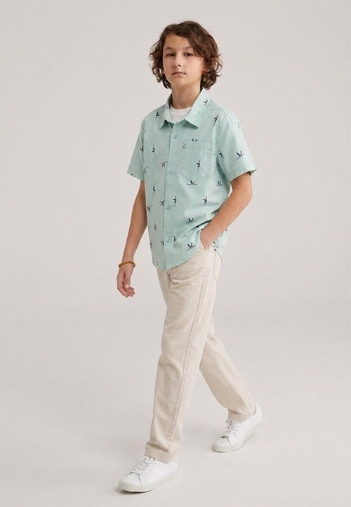 A kid wearing a light mint green kids short-sleeve button-down shirt showing the subtle, repeating small bird print.