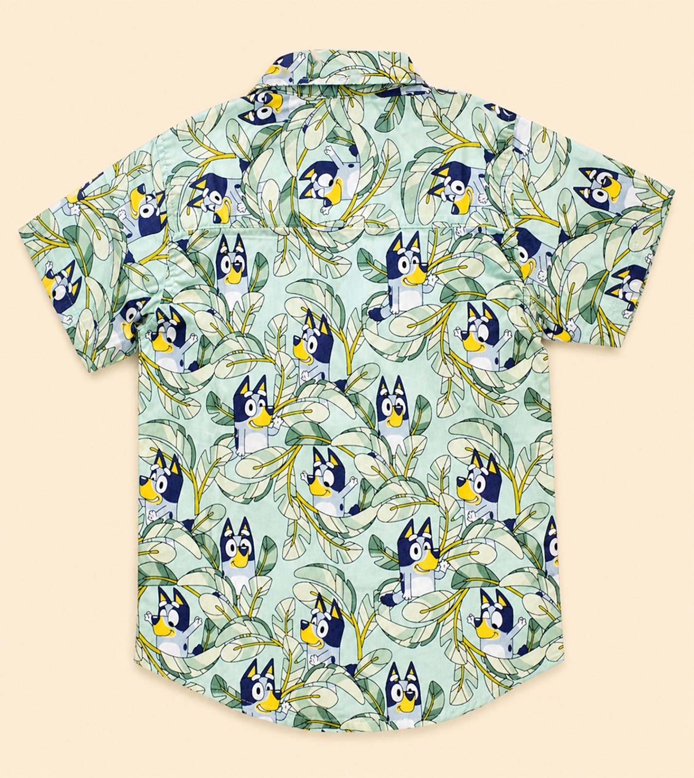 Two Moons Canada kids short-sleeve button-down shirt back side featuring a cartoon blue dog and tropical green leaves on a mint background.