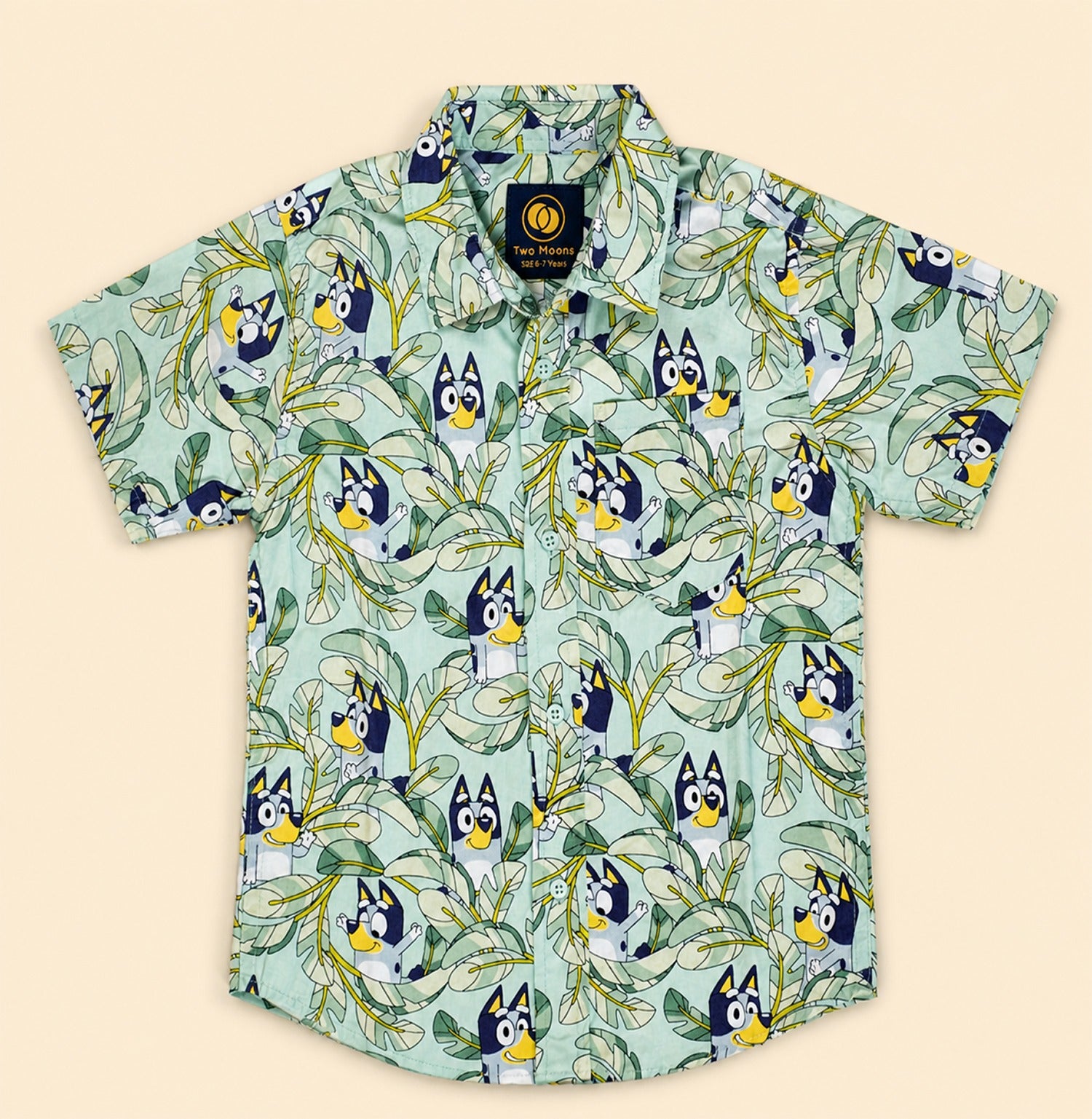 Two Moons Canada kids short-sleeve button-down shirt front side featuring a cartoon blue dog and tropical green leaves on a mint background.