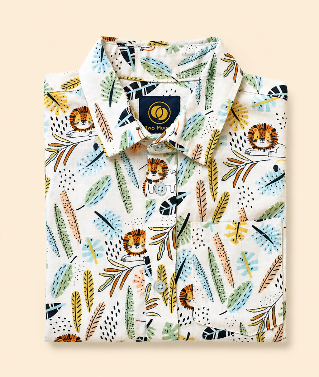 Neatly folded white kids button-down shirt highlighting the colorful safari lion and jungle leaf pattern.