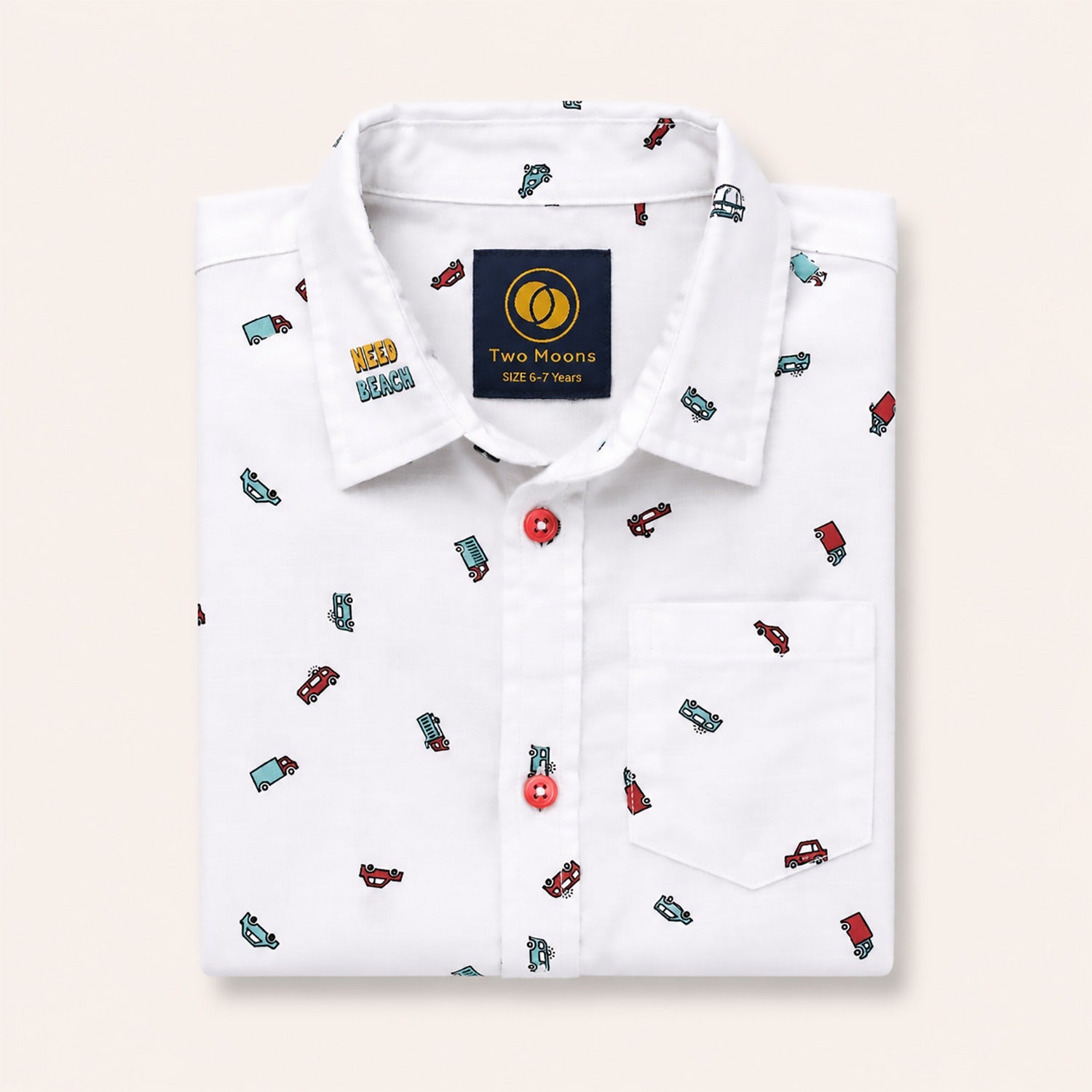 Neatly folded white kids button-down shirt highlighting the colorful car and truck motifs and contrasting red buttons.