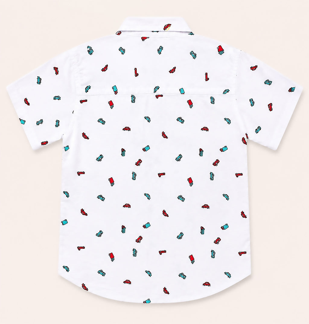 Back view of a white kids short-sleeve button-down shirt showcasing the playful, repeating multi-colored vehicle print.