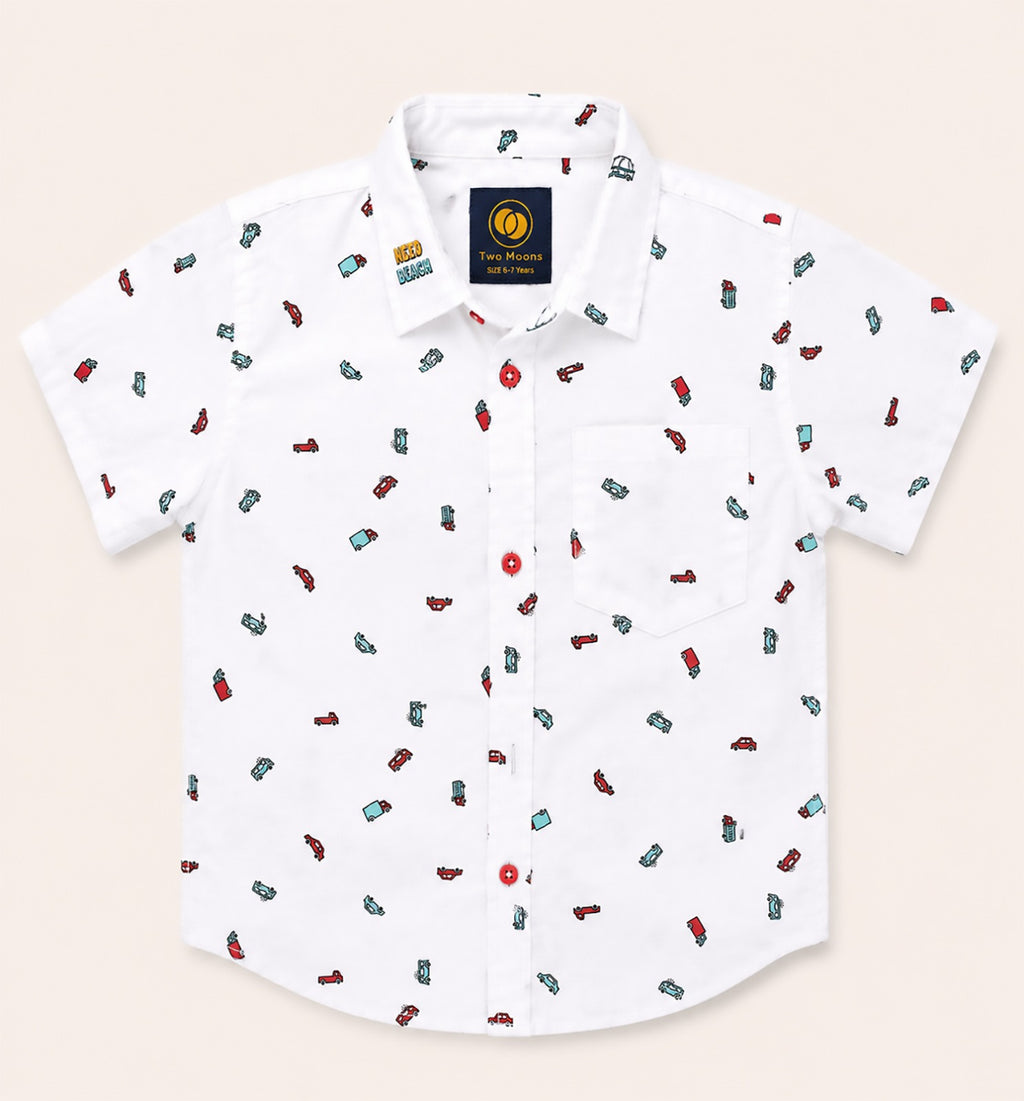 Front view of a white kids short-sleeve button-down shirt featuring a colorful pattern of toy cars and trucks with bold red buttons.