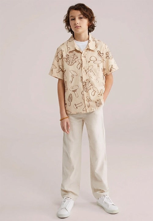 Two Moons Canada kid wearing a short-sleeve button-down shirt featuring a brown vintage botanical mushroom print on a beige background.
