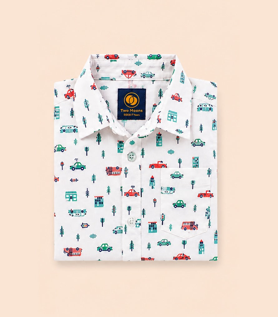 Neatly folded white kids button-down shirt highlighting the colorful car, house, and tree motif along with classic clear buttons.